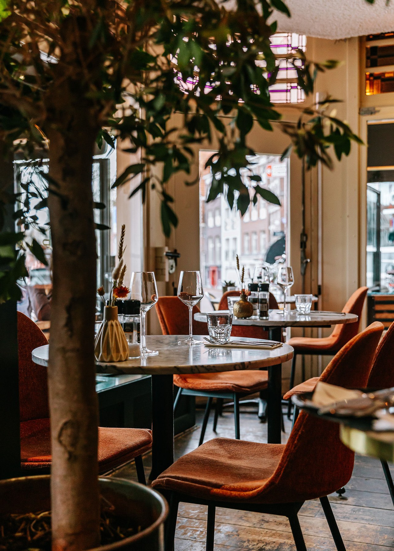 Marmeren tafels, groene planten en warme stoelen in het restaurant